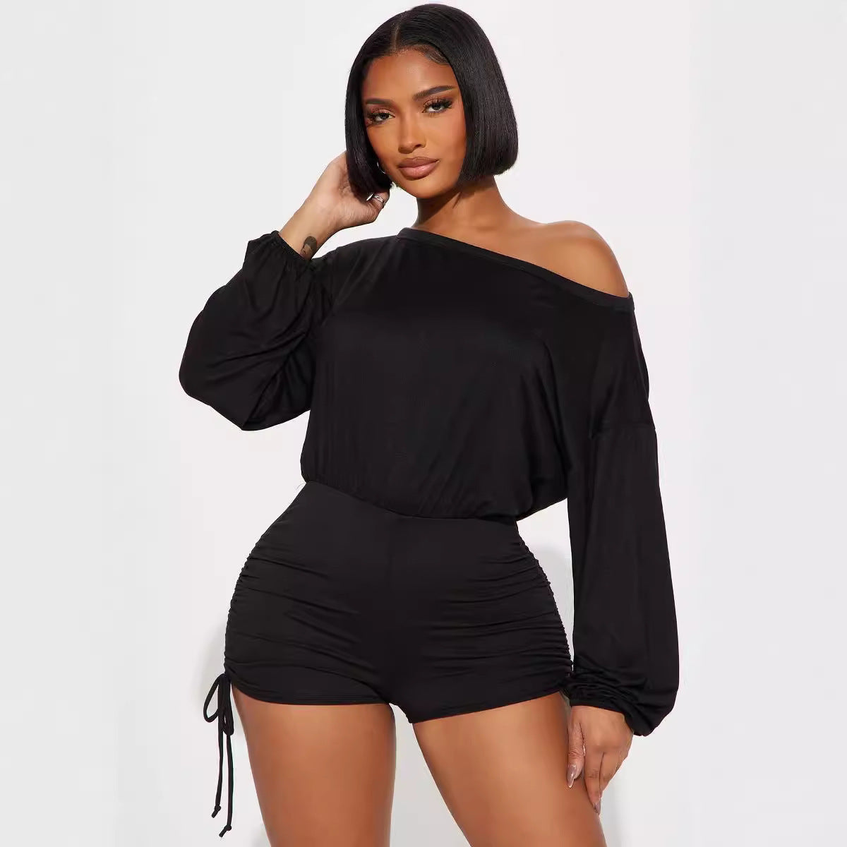 Woman wearing black off-shoulder long sleeve jumpsuit with diagonal collar and pleating design