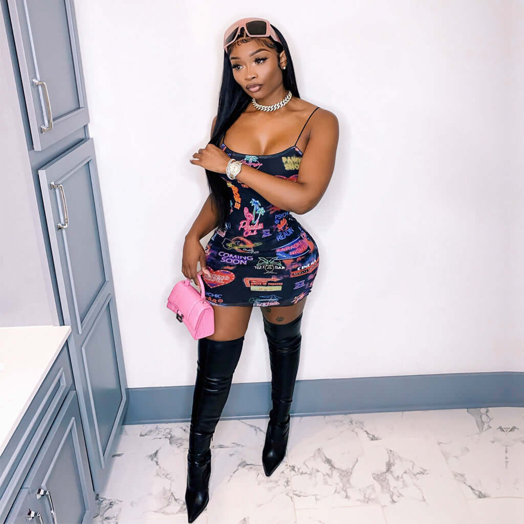 Woman wearing a printed collage splicing bodycon mini dress with spaghetti straps and thigh-high black boots, holding a pink purse.