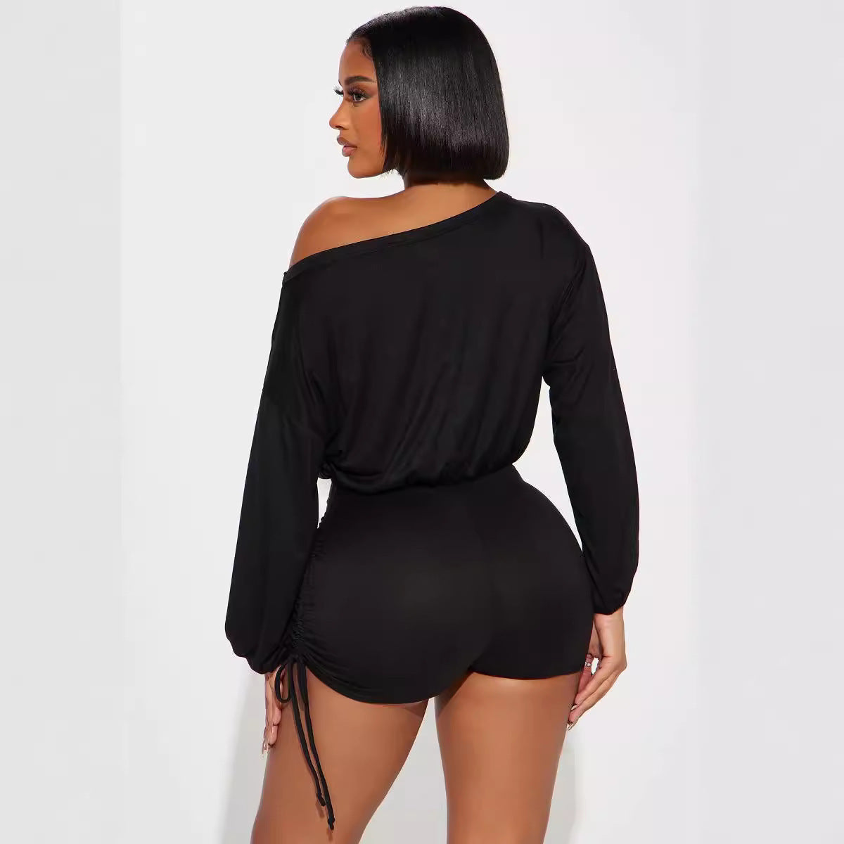 Woman wearing black off-shoulder long sleeve loose jumpsuit with diagonal collar and pleating design