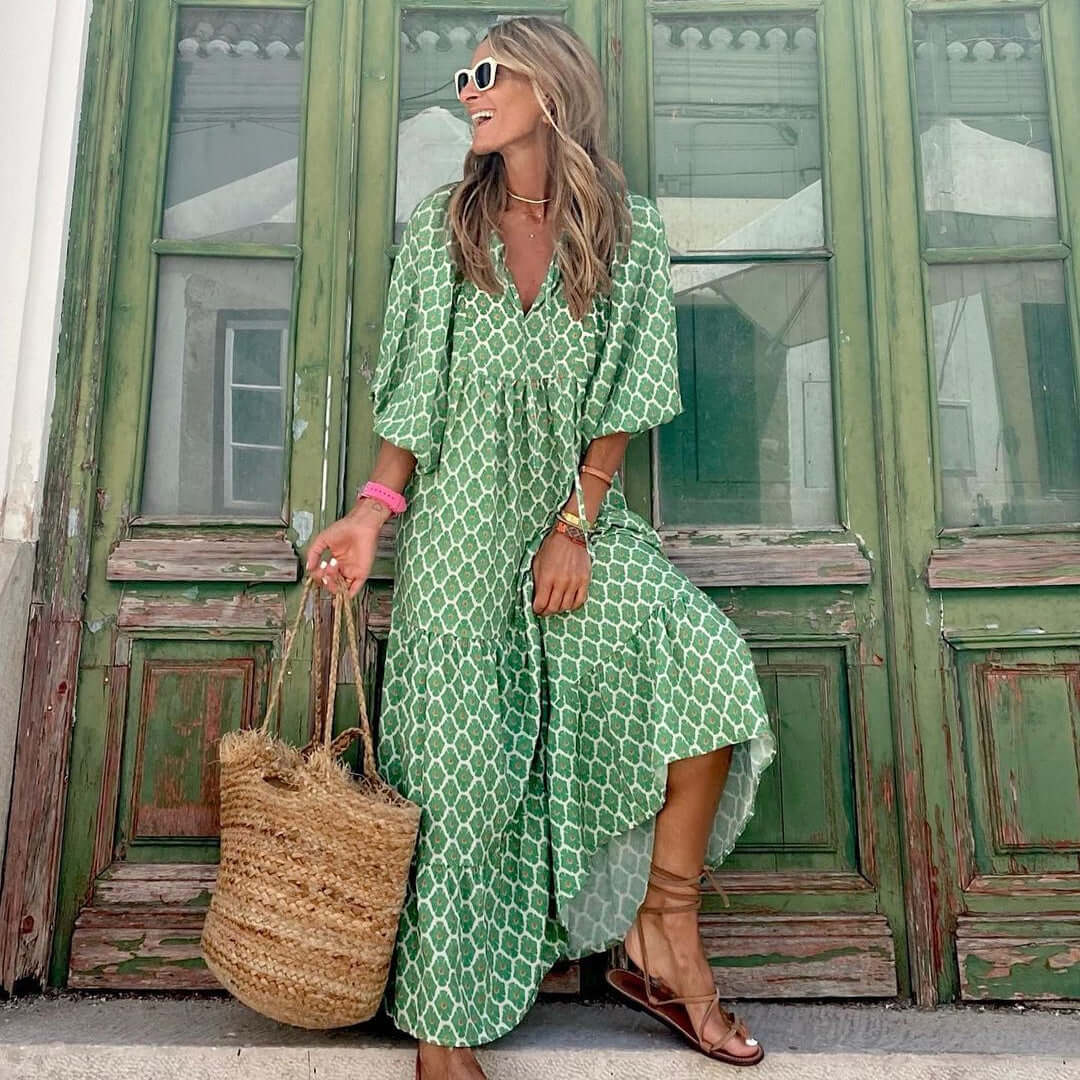 woman wearing green British style vintage floral bohemian maxi dress with V-neck and short sleeves standing by rustic green door carrying straw tote bag