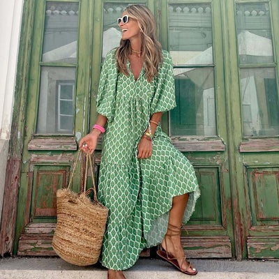 woman wearing green British style vintage floral bohemian maxi dress with V-neck and short sleeves standing by rustic green door carrying straw tote bag