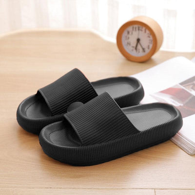 Black bathroom sandals on wooden floor with clock in background.